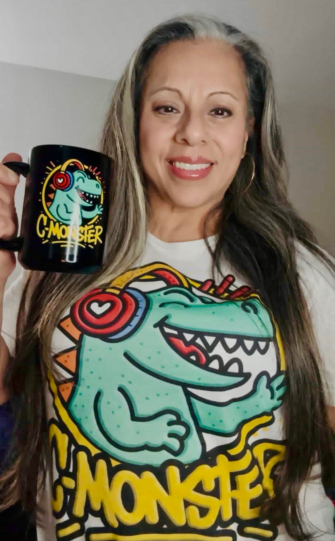 Person wearing a t-shirt with a colorful monster graphic and holding a black mug with a similar design.