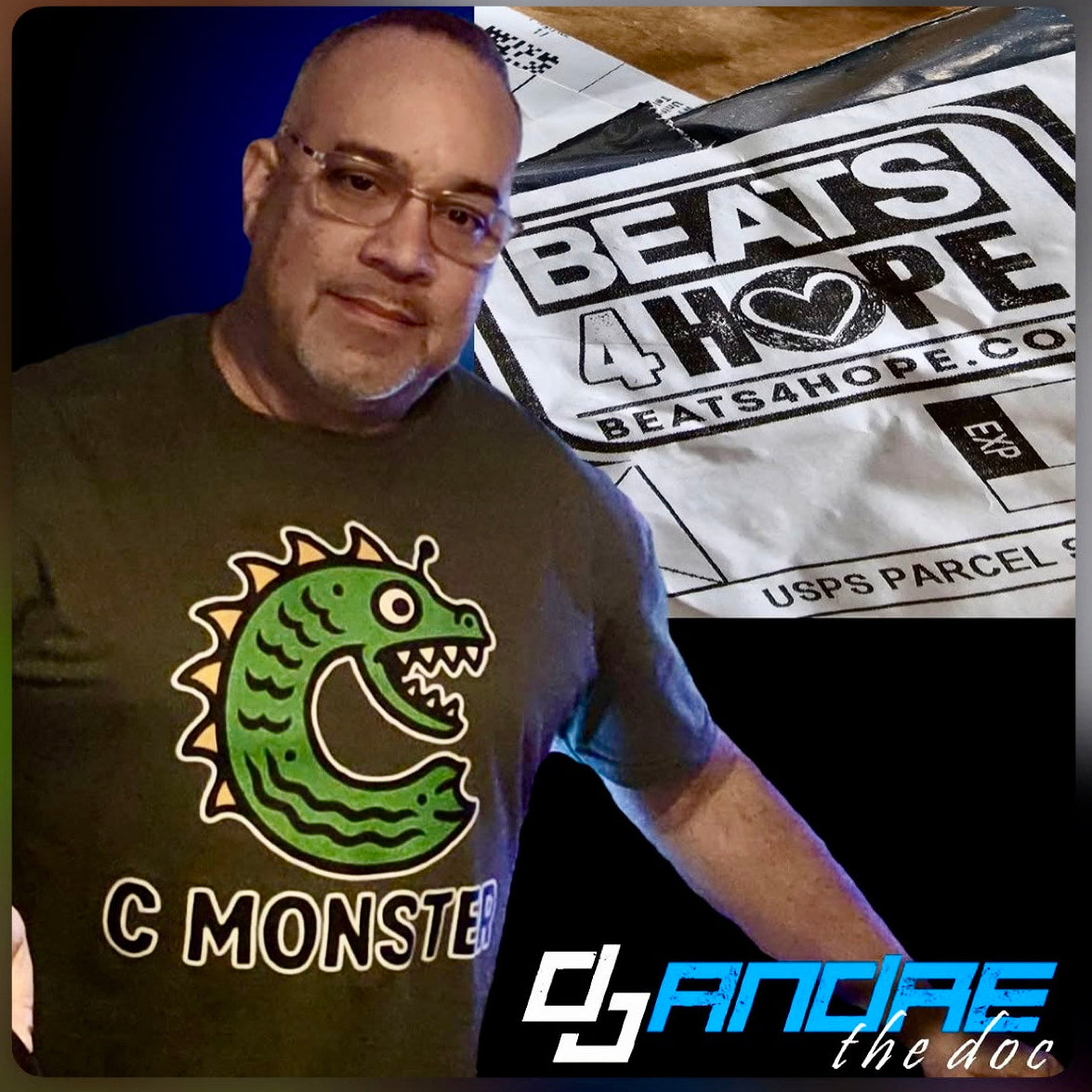 Man wearing a t-shirt with a green monster design, standing next to a 'Beats 4 Hope' poster.