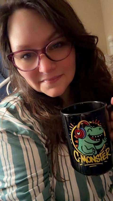 Person holding a black mug with a colorful design, wearing glasses and a striped shirt.