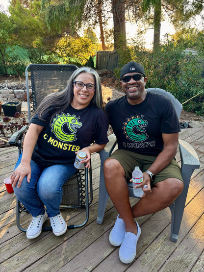 Two people sitting outdoors on a wooden deck, wearing matching black t-shirts with a green logo.