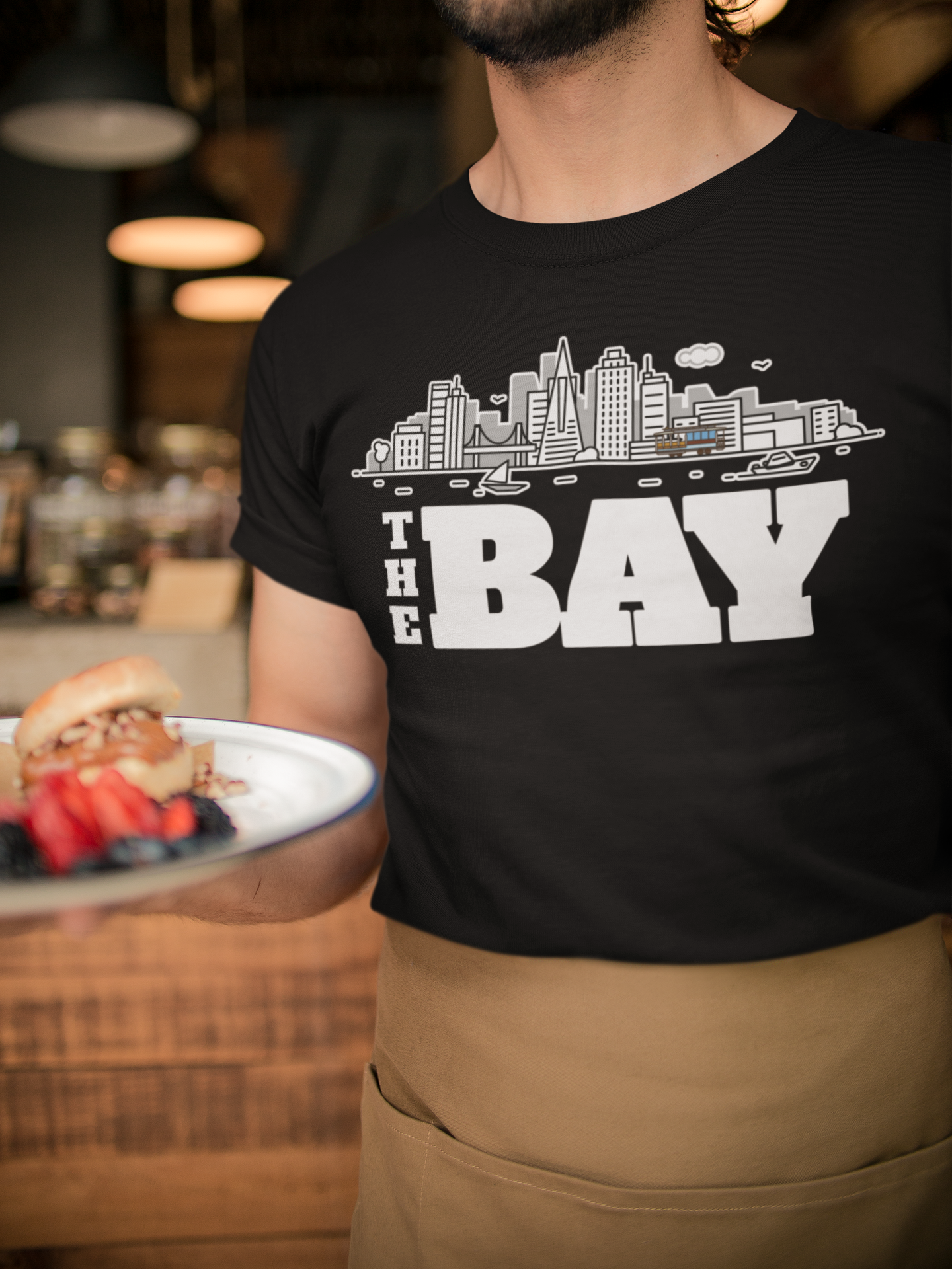 Person wearing a black t-shirt with 'The Bay' design, holding a plate of food.